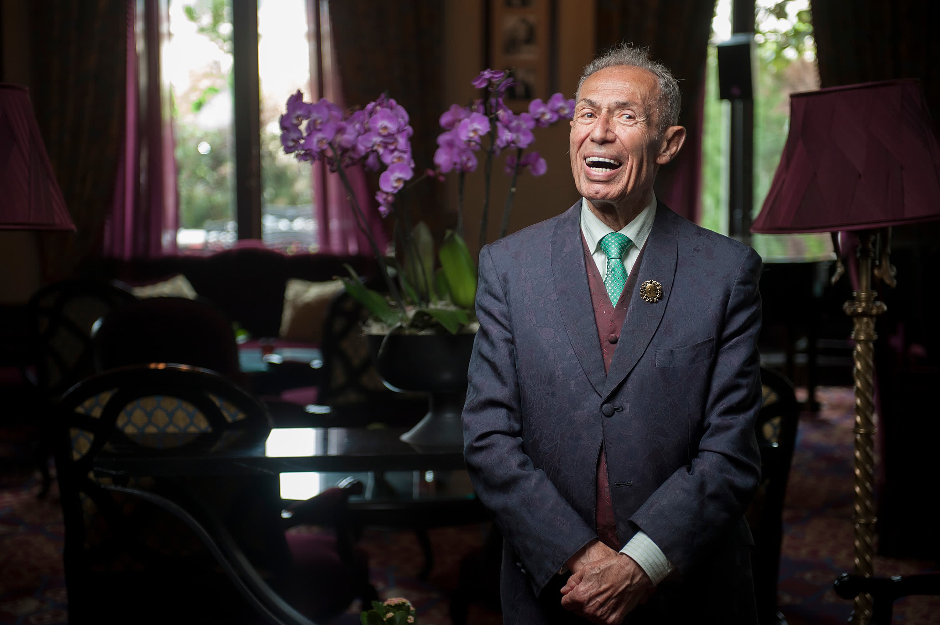 A man in a suit laughing in a dim room with purple orchids