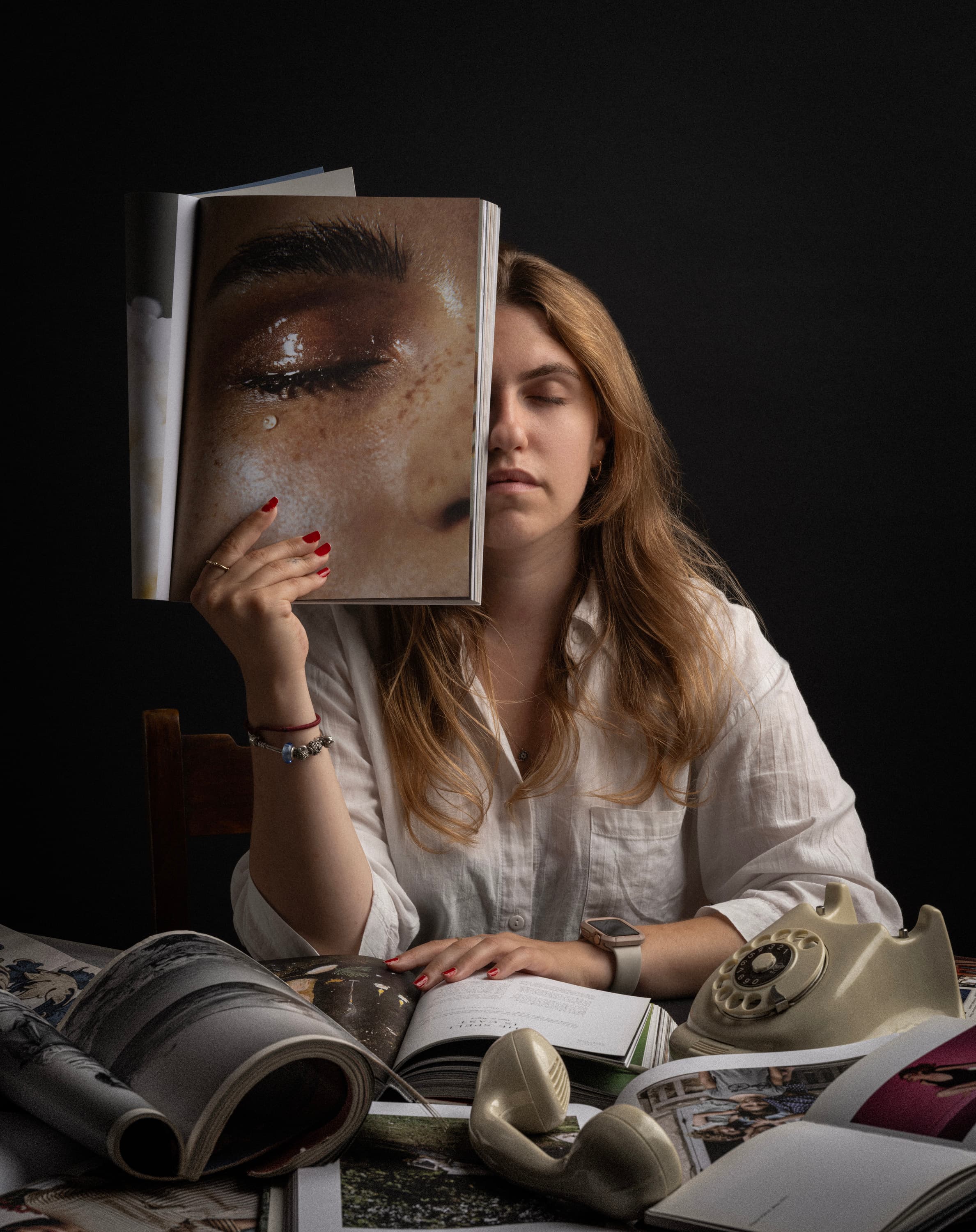 A seated woman holds an open magazine in front of her face