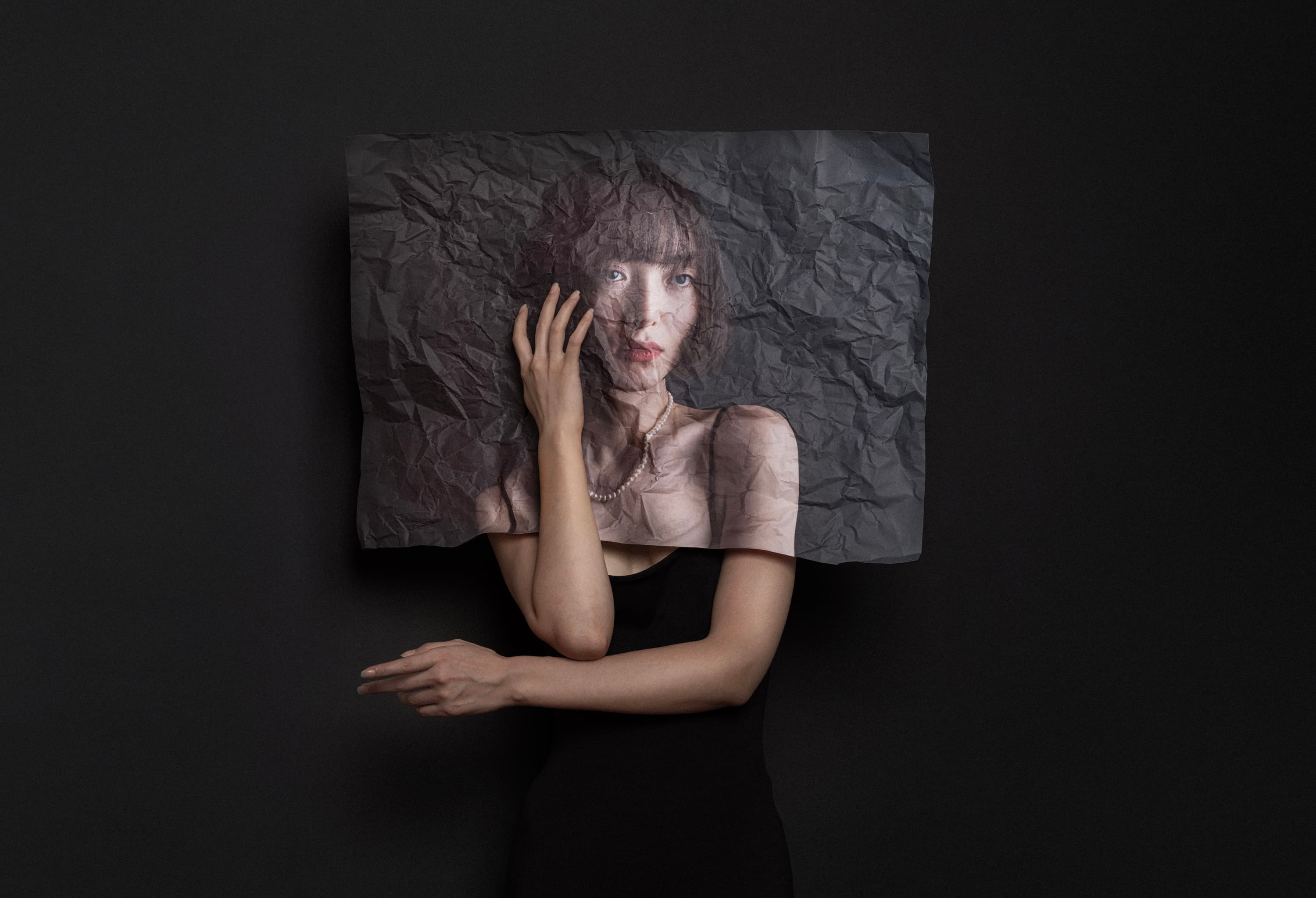 A woman's portrait printed on crumpled paper held in front of her face
