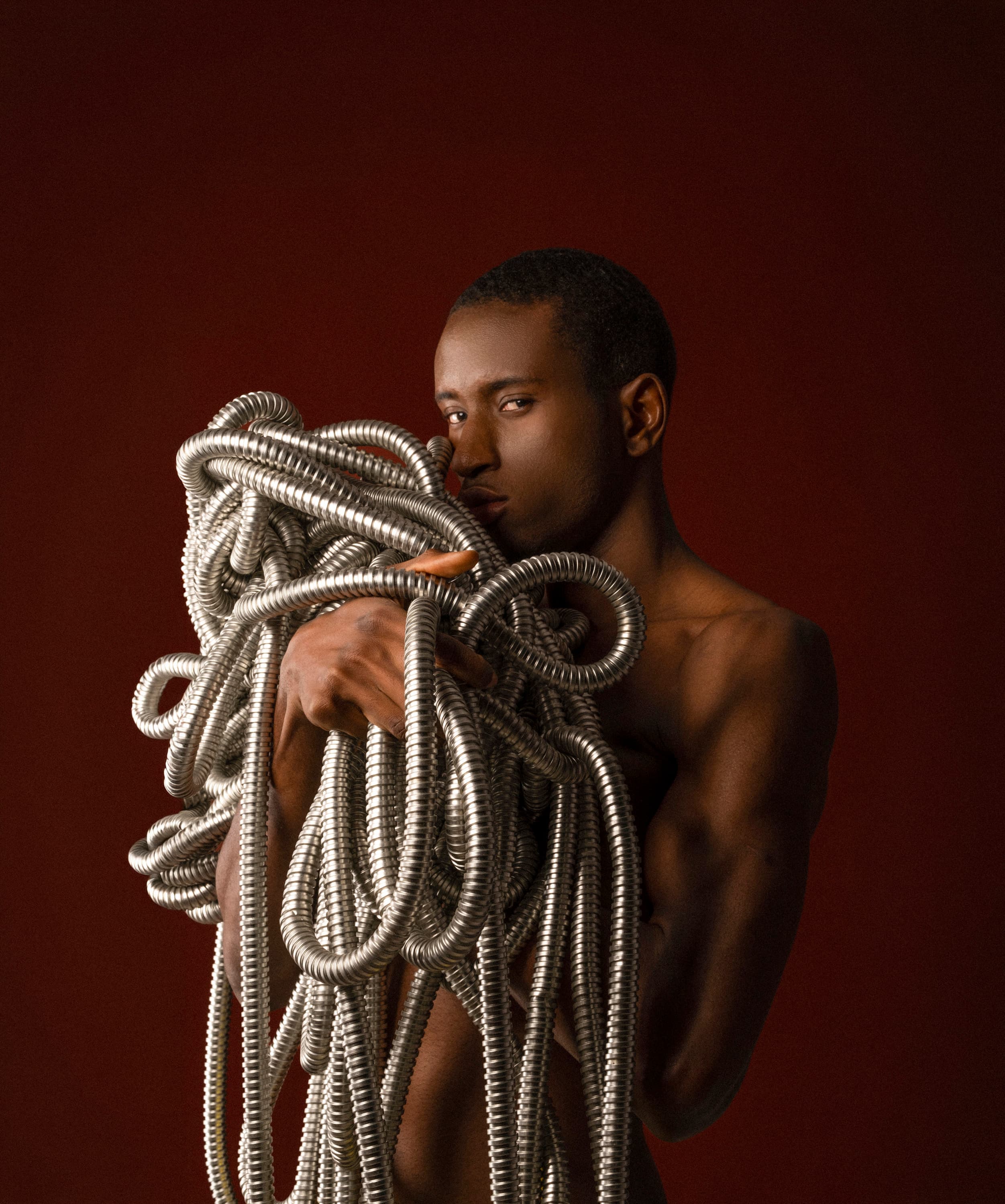 A man embraces a tangle of silver flexible tubing against a deep red background
